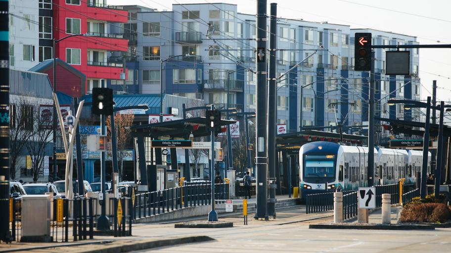 A street-level light rail station, with a blue-and-white train stopped at the platform