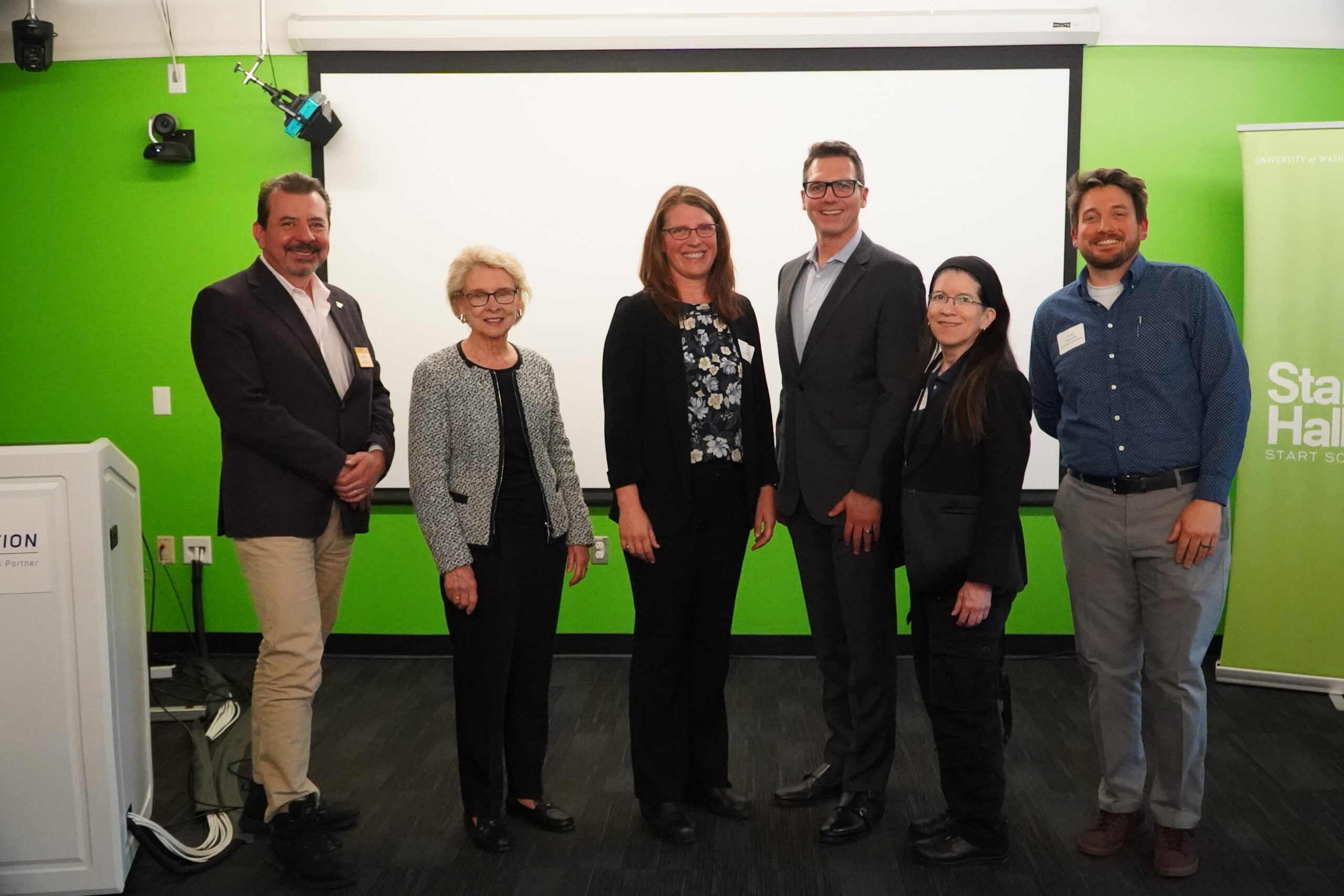 Six leaders, including François Baneyx (UW), Chris Gregoire, Carrie Sturts Dossick, Bart Treece, Cecilia Aragon, and Travis Thonstad, pose together in front of a presentation screen at a 2026 event.