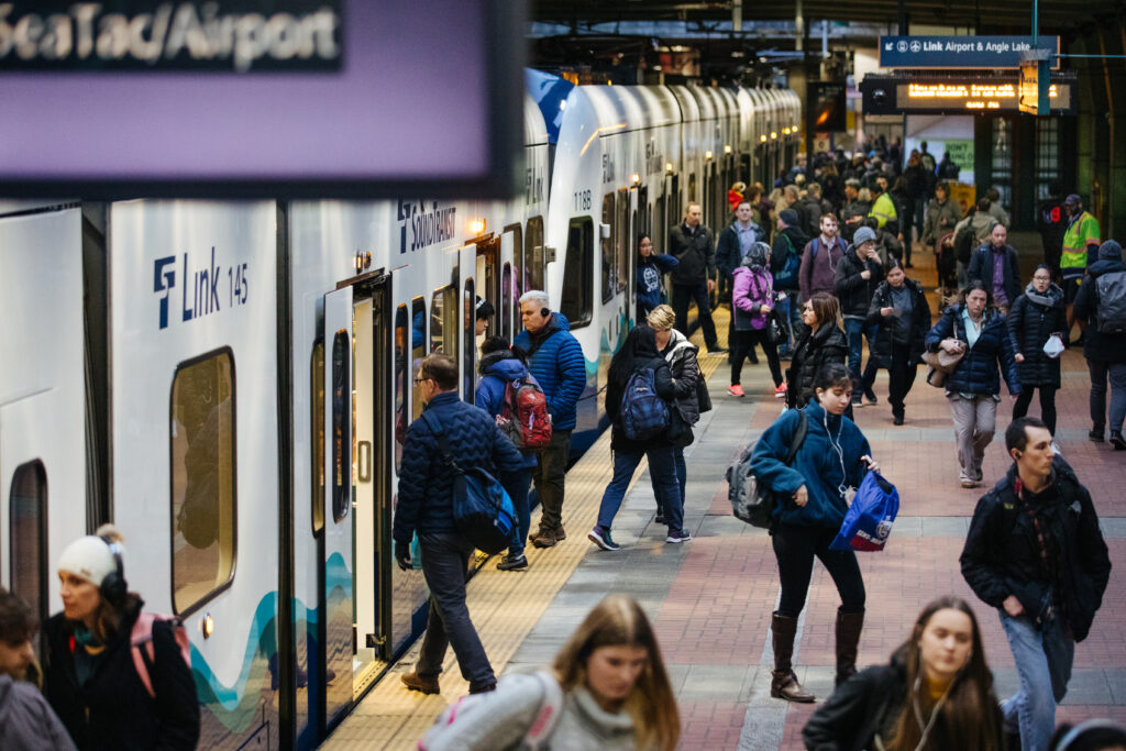 Passengers boarding and walking beside a Sound Transit Link light rail train at a busy station platform.
